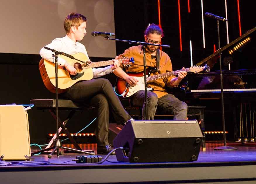 Two guitarists performing a duet together on stage at a recital